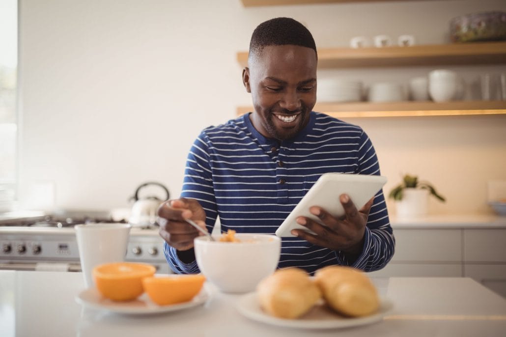 Das Bild zeigt einen neuen Mitarbeiter, der sein Preboarding zuhause beim Frühstück am Tablet absolviert.