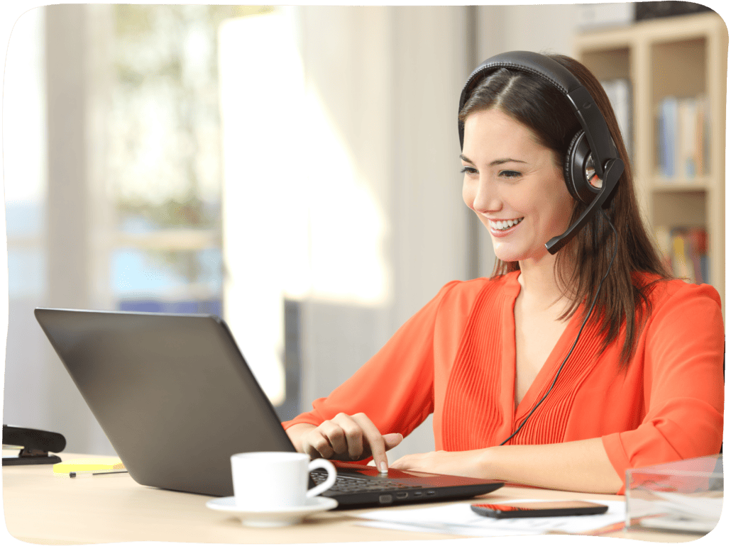 Eine Frau sitzt lächelnd vor einem aufgeklappten Laptop und telefoniert mit einem Headset.