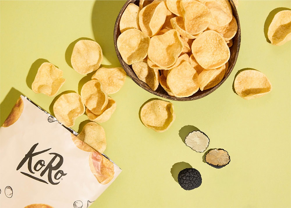 Das Bild zeigt ein Produktbild von KoRo - ein Kunde von elearnio. Man sieht eine ausgeschüttete Tüte mit Chips wie einen aufgeschnittenen Trüffel. Der Hintergrund ist hellgrün und die Objekte haben einen harten Schlagschatten.