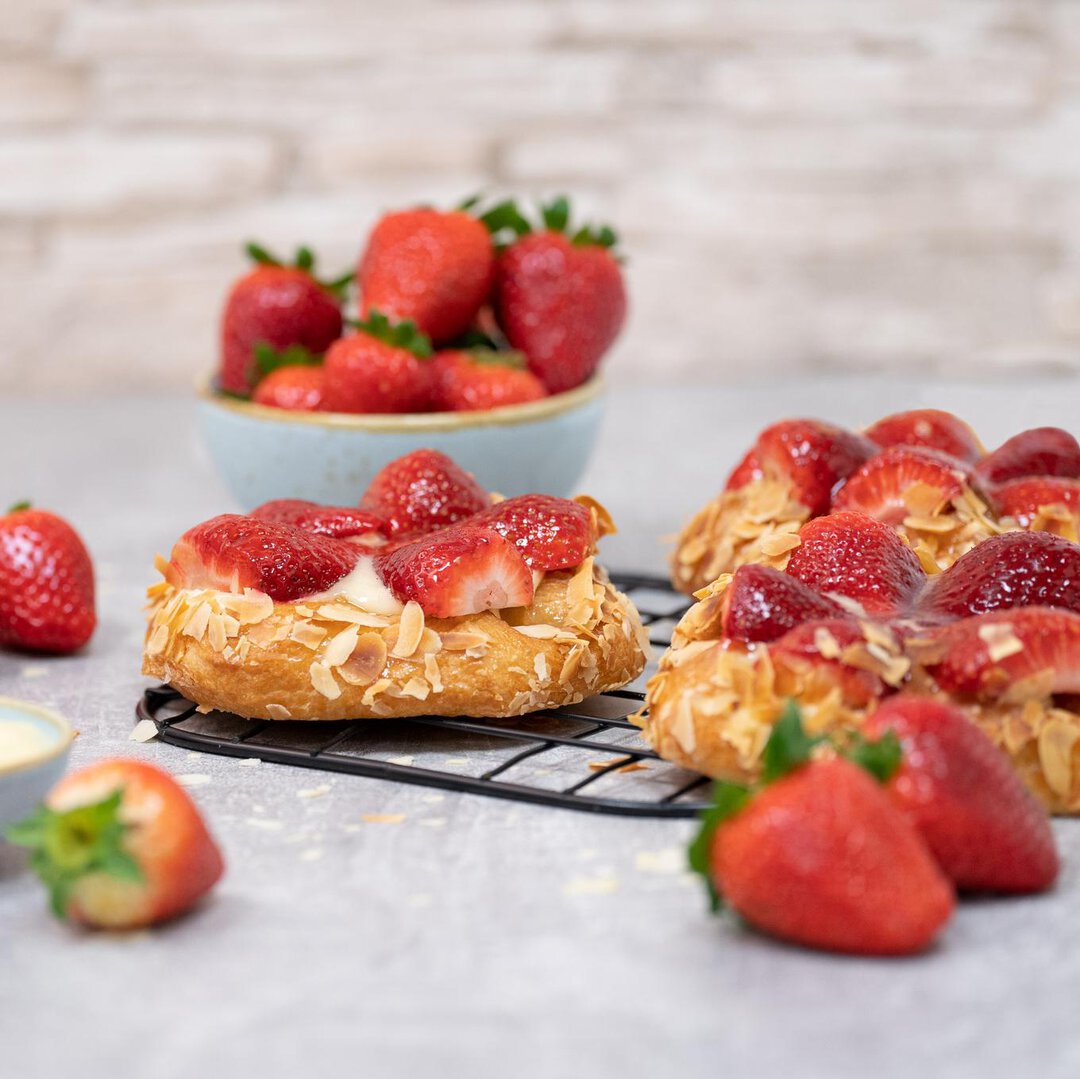 Frontalaufnahme von Erdbeerplundern auf einem Backgitter umgeben von Erdbeeren.