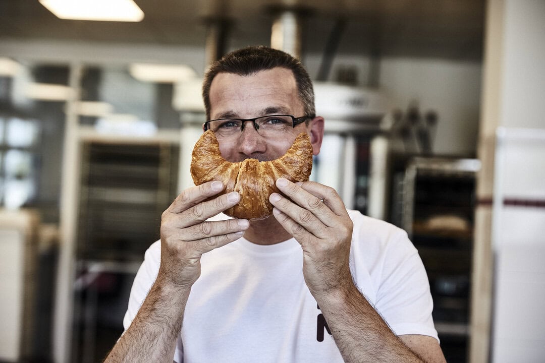 Produktionsmitarbeitender bei MALZERS Backstube hält ein Croissant vor sein Gesicht.